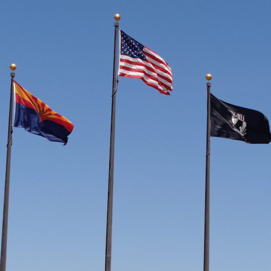 The Arizona flag, the American flag and the POW/MIA flag flying against a clear blue sky
