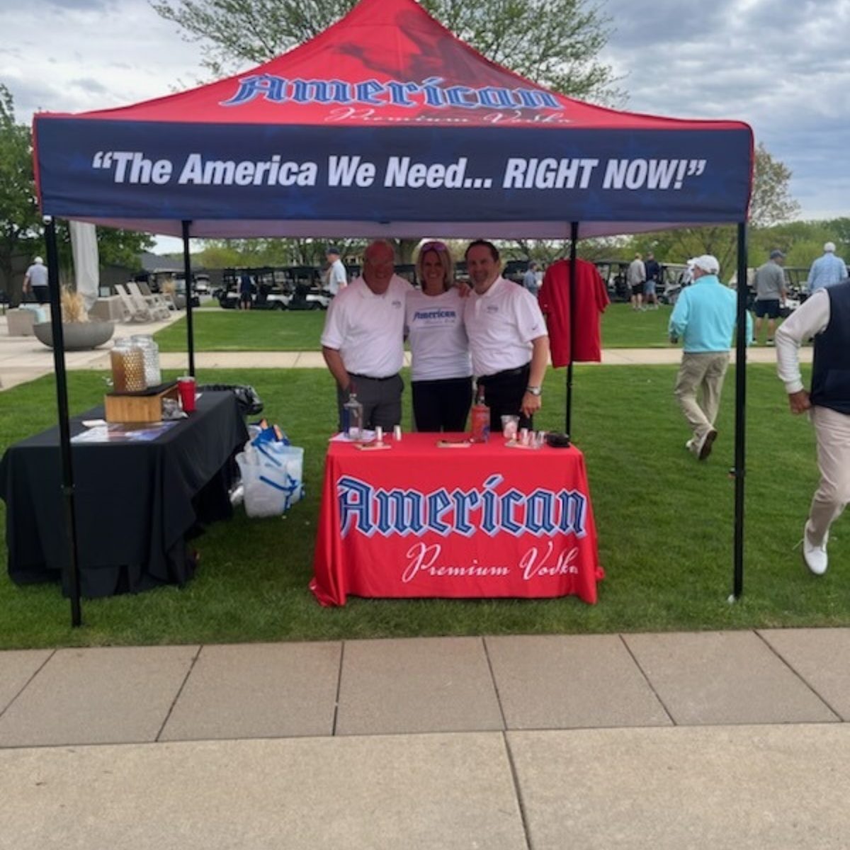 Three team members under a red American Premium Vodka tent at a golf tournament